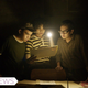 Three boys stare at a paper illuminated by a flashlight.